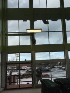 Worker washing tall commercial windows beside a glass entrance on a rainy day